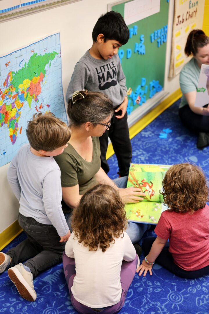 kids surrounding a teacher who is holding a children’s book